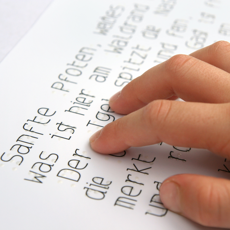 Hand reading text with braille and printed characters